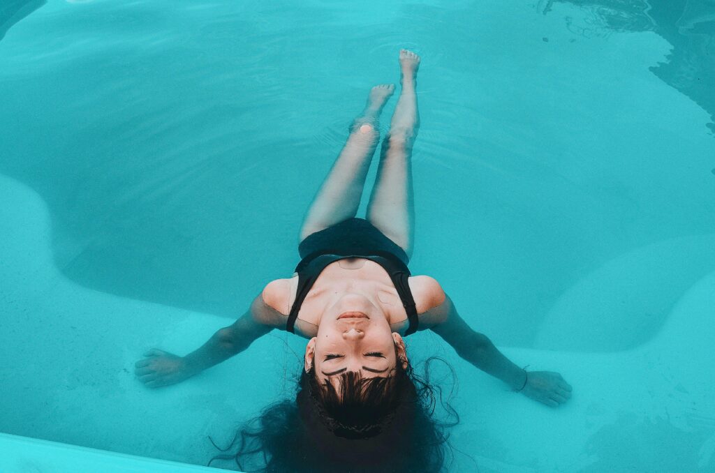 A woman in a black swimsuit floats gracefully in a serene swimming pool.
